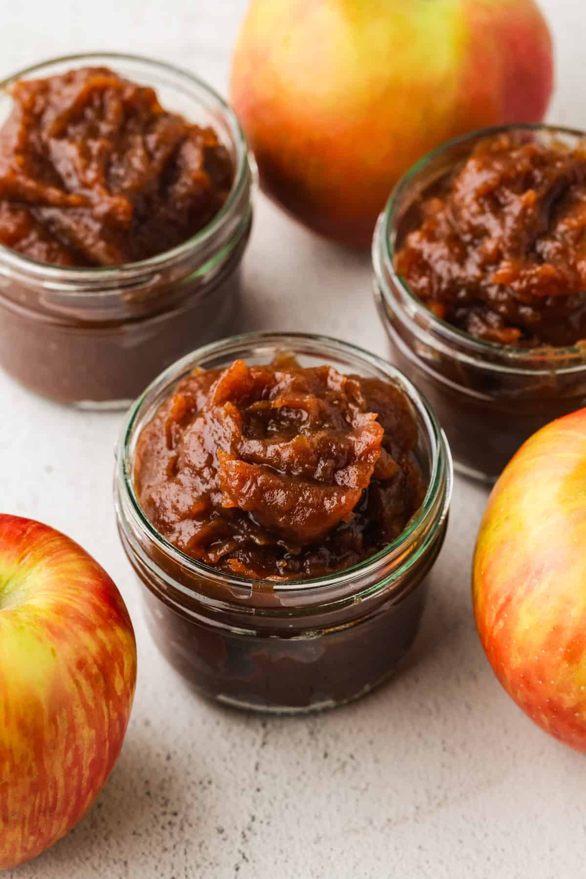 Small glass jars filled with homemade spiced apple butter with apples nearby.