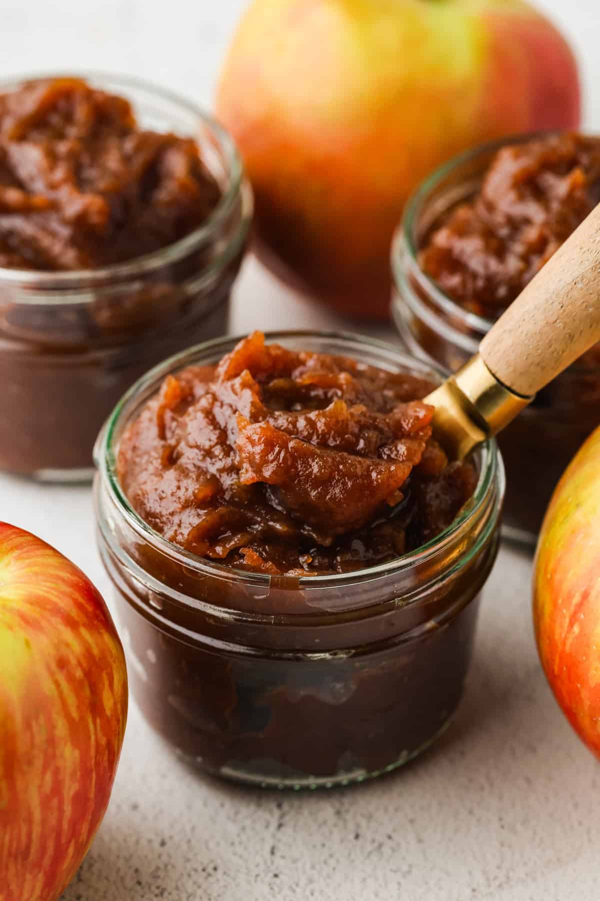 A spoon scooping up some apple butter from a small glass jar.