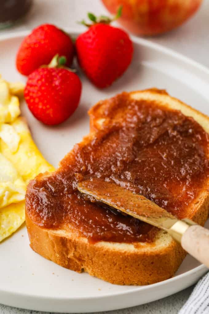 A knife spreading some apple butter on a piece of toast.