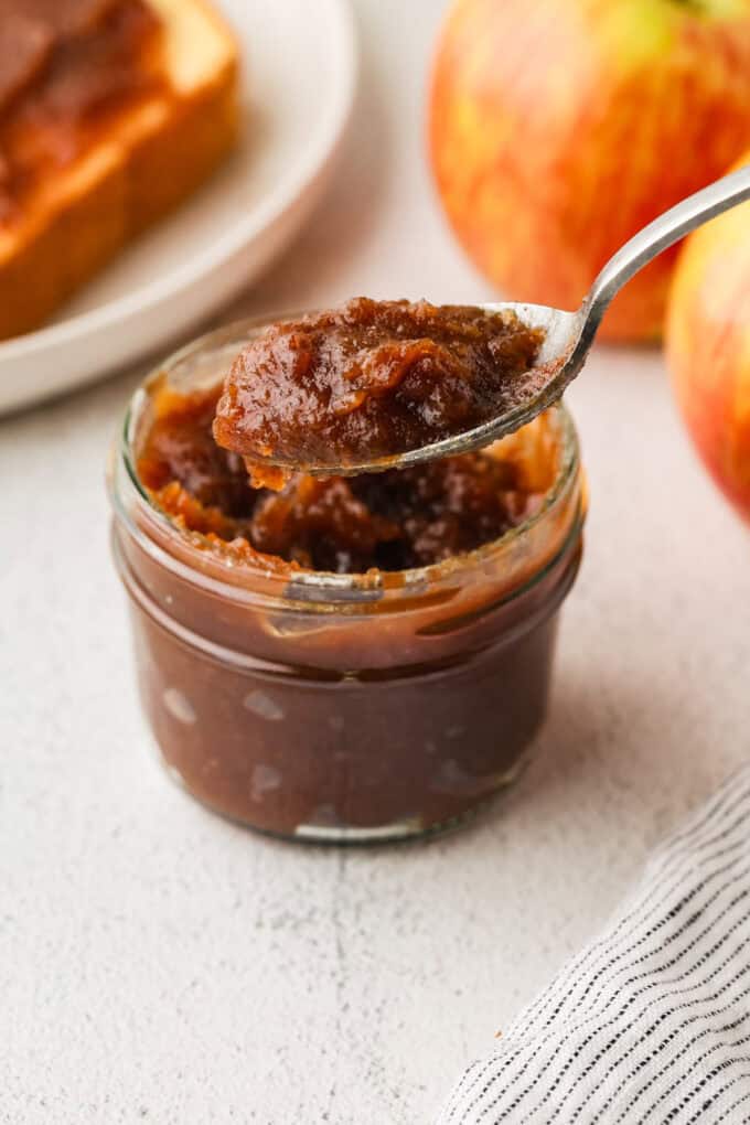 A spoonful of apple butter lifted from a small glass jar.