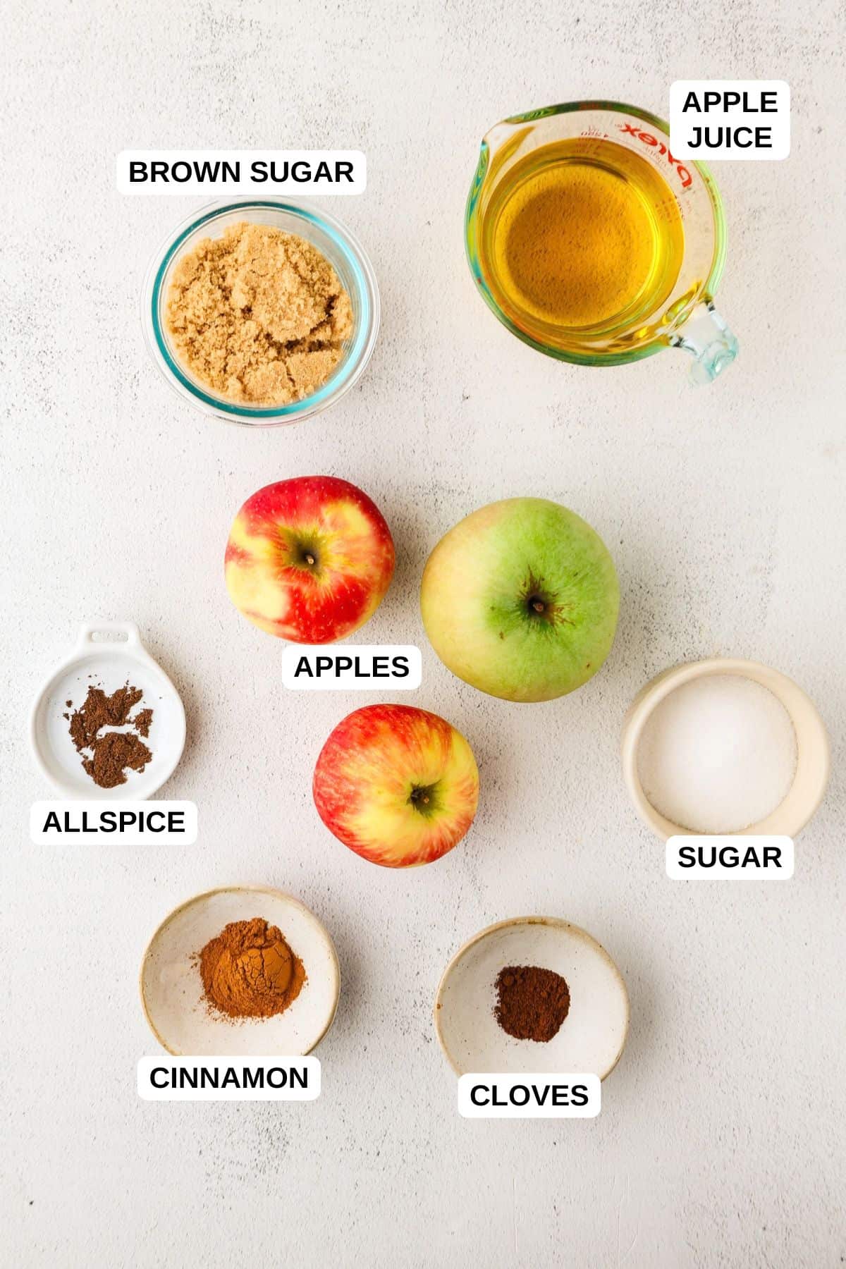 Ingredients laid out in separate bowls around some apples for a recipe for apple butter.