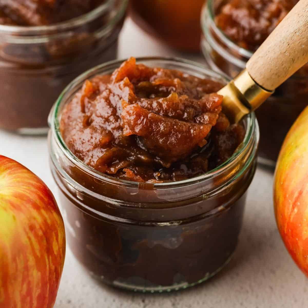 Close up of a spoon scooping up some apple butter from a small glass jar.