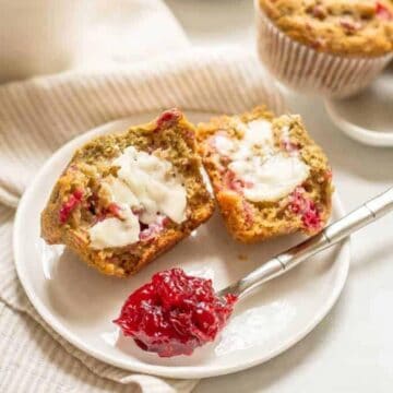 Whole wheat cranberry sauce muffin split in half, smeared with butter and served on a small white plate